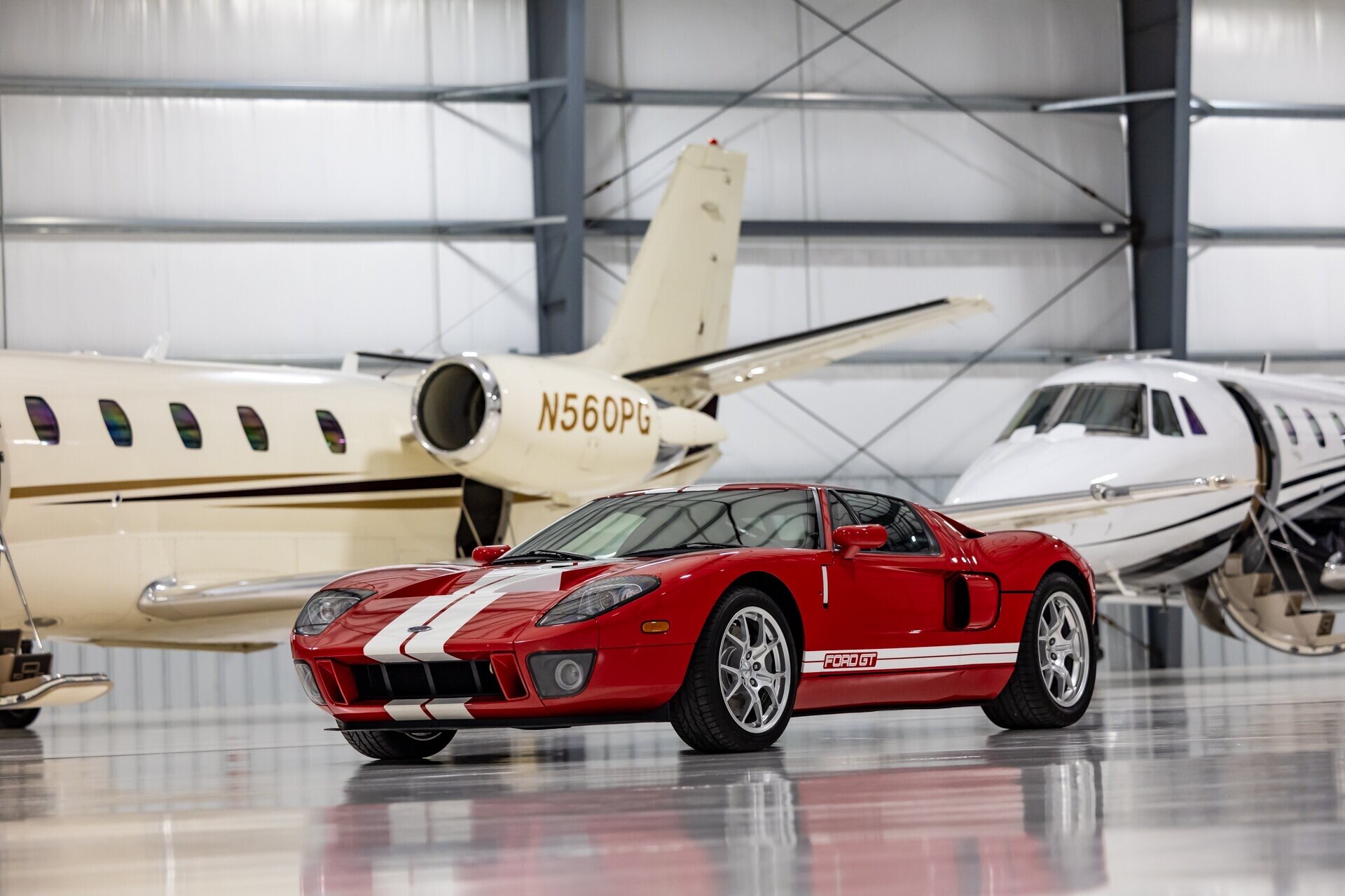 Red Ford GT parked in front of private jets in a hangar