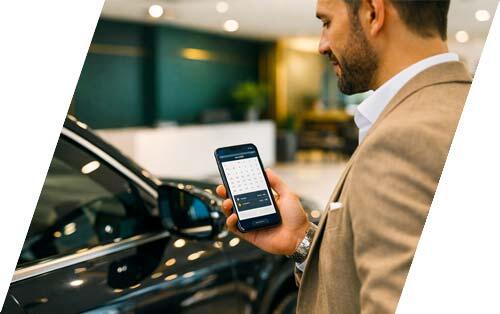 Well-dressed customer scheduling a test drive on a smartphone beside a luxury vehicle inside a modern dealership